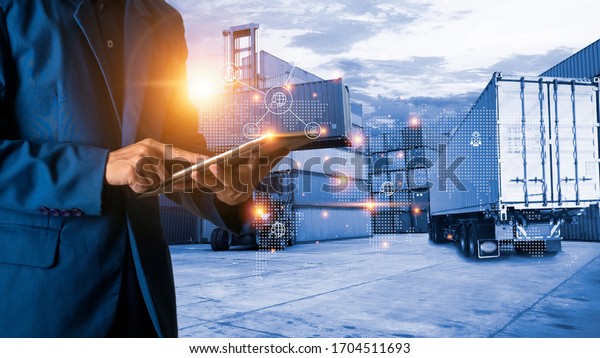 Global logistic or world of logistic concept.\
Businessman or manager using tablet standing with world map icon\
and shipping yard container and truck of transport background. fast\
or instant shipping.