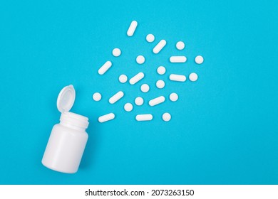 Global Pharmaceutical Industry And Medicinal Products - White Pills Or Tablets Scattered From The Pill Container, Lying On Blue Background