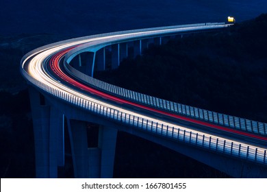 Global transport and logistics connection. Heavy traffic on the modern and futuristic highway. High curved bridge, engineering masterpiece in the sunset.