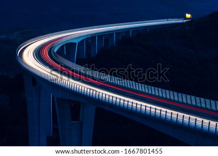 Global transport and logistics connection. Heavy traffic on the modern and futuristic highway. High curved bridge, engineering masterpiece in the sunset.