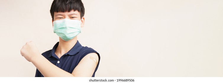Global Vaccination Race Against Covid 19 Concept. Studio Portrait Of A Healthy Asian Teen Boy With Face Mask Proudly Present The Band Aid On His Arm For First Dose Vaccine Against Coronavirus. Safe