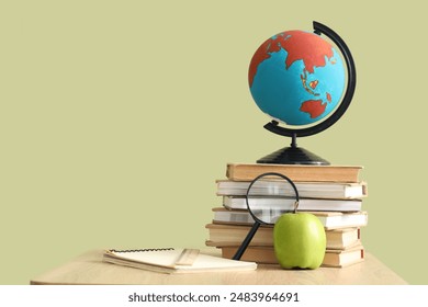 Globe with books, magnifier and apple on desk against green background - Powered by Shutterstock