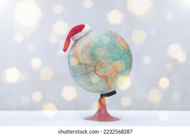 globe with christmas hat on snow. bokeh flare Santa Claus Hat on ball. Christmas international travel concept - Powered by Shutterstock