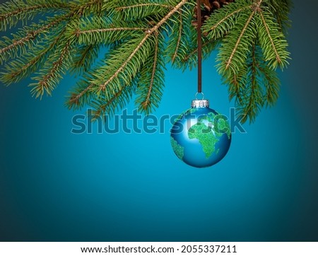Globe christmas ornament hanging from a tree branch on blue. Peace on Earth, eco friendly or winter travel concept.