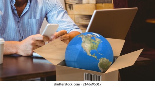 Globe In Delivery Box Against Mid Section Of A Person Using Smartphone In A Cafe. Logistics And Transportation Business Concept