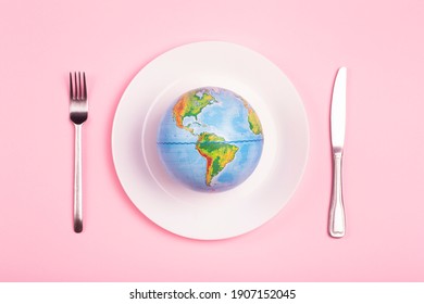 Globe on a plate for food on a pink background. Power, economy, politics, globalism, hunger, poverty and world food concept.