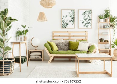 Globe shaped lamp placed on wooden table standing next to green couch in stylish living room interior