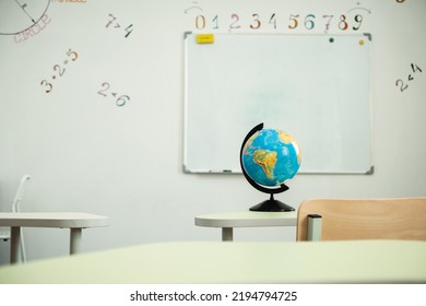 The Globe Stands On The Desk In The School Classroom Against The White School Board. Planet Earth. Back To School Concept. Classroom Interior Design