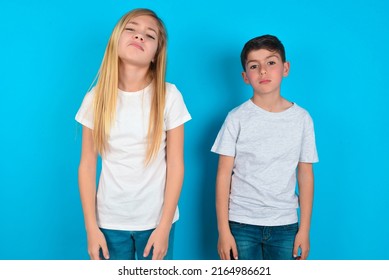 Gloomy, Bored Two Kids Boy And Girl Standing Over Blue Background Frowns Face Looking Up, Being Upset With So Much Talking Hands Down, Feels Tired And Wants To Leave.