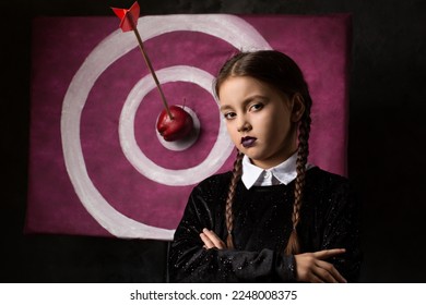 A gloomy girl with pigtails near a target with an arrow and an apple in a gothic style on a dark background - Shutterstock ID 2248008375