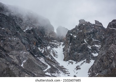 Gloomy mountain landscape with high sharp rockies with snow in gray low clouds. Closeup of sharp rocks and peaked tops in gray cloudy sky. Bleak overcast scenery with mountain range with pointy rocks. - Shutterstock ID 2102607685