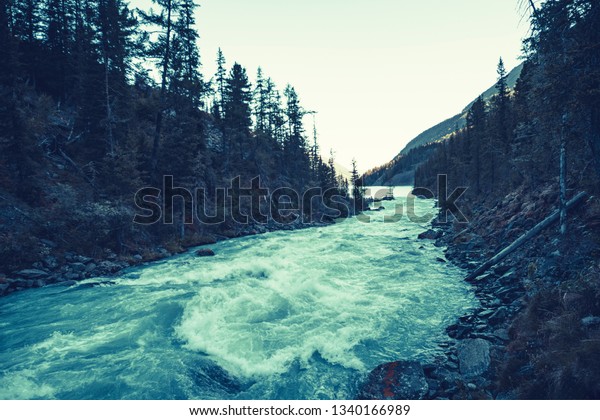 Gloomy mountain landscape with river on opposite\
bank. Stony bank of river. Dark green color of water. Eerie\
atmosphere in overcast rainy weather in cinematic faded tones.\
Horror style.