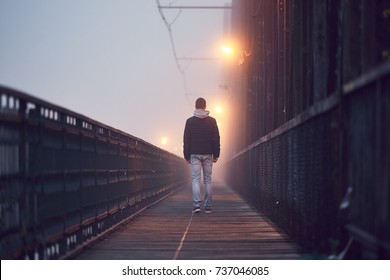 Gloomy weather. Lonely man is walking on the old bridge in mysterious fog.