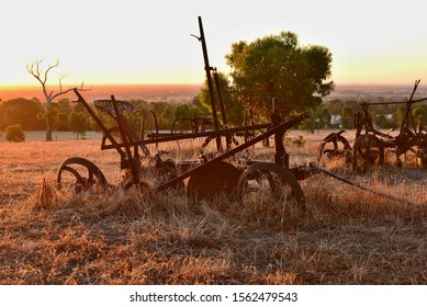 Glorious Summer Landscape Drenched With Sunset. Ranch - Old Rusted Farm Machinery Illuminated By Warm Orange Light. Dry Grass And Typical Australian Landscape Around. Equipment Forgotten In Time.