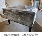 Glossy black grand piano partially covered in plastic wrap in preparation for removal by furniture moving company