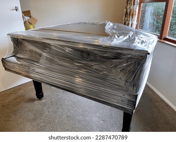 Piano de piano de cola negro brillante parcialmente cubierto de envoltura de plástico como preparación para la remoción por parte de la empresa de mudanza de muebles