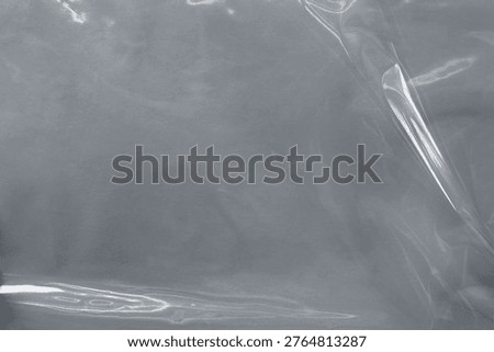 Glossy, transparent plastic wrap texture with a smooth, reflective surface in shades of gray, creating a sleek, modern background.