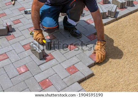 A gloved craftsman lays down the paving stones in layers. Laying gray concrete paving slabs in the courtyard of the house on a sandy foundation.