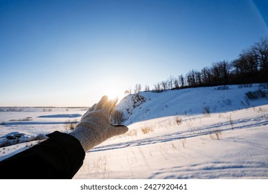 A gloved hand blocks the sunlight in winter, the glare of the setting sun shows through his fingers. Winter landscape, the beauty of Russia's nature. High quality photo - Powered by Shutterstock