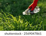 Gloved hand collecting an empty plastic bottle in a sunlit meadow, highlighting the importance of environmental responsibility and community cleanup efforts for a cleaner planet. Ecology, earth day