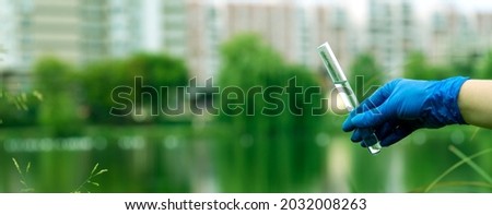 A gloved hand collects water into a test tube. Sampling from open water in a city water body. Scientist or biologist taking a sample of water in a test tube against the background of a cityscape.