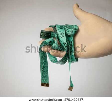 Gloved hand constrained by a tangled, green fiber-glass measuring tape, signifying measure.