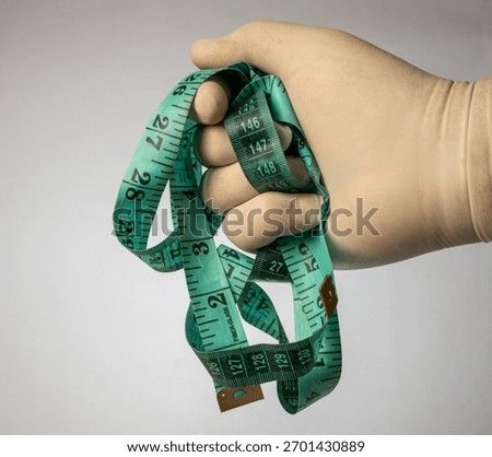 Gloved hand constrained by a tangled, green fiber-glass measuring tape, signifying measure.