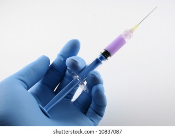 gloved hand with filled blue syringe with needle