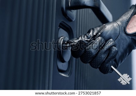 Gloved hand inserting keys into apartment door lock, opening or closing entrance. Suspenseful concept of burglary, illegal access, anonymous intruder or squatter entering property without fingerprints. Photo