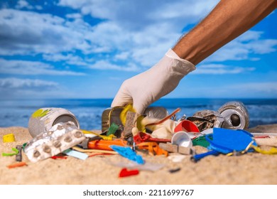 A Gloved Hand Picking Up Litter On A Trashed Beach 