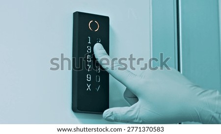 A gloved hand presses a button on a digital lock in a sterile laboratory environment, emphasizing precision and cleanliness essential in biotechnology and healthcare settings.