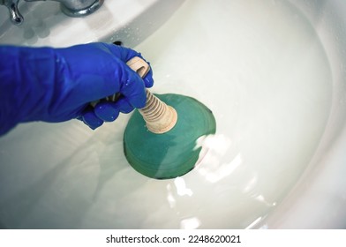 Una mano engullida con un émbolo de goma, golpeando un bloqueo en el lavabo. Llame al plomero maestro. El agua del cuarto de baño no desaparece.
