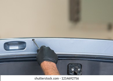 A Gloved Hand Spraying Rust Proofing Into A Small Hole In The Hatch Of A Vehicle.