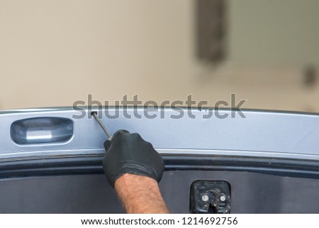 A gloved hand spraying rust proofing into a small hole in the hatch of a vehicle.