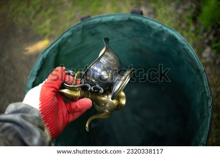 A gloved hand takes antique dishes out of the trash can.A valuable find in the trash.Throw the antiques in the bucket.