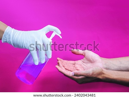 a gloved hand that sprays hand sanitizer on the other hand