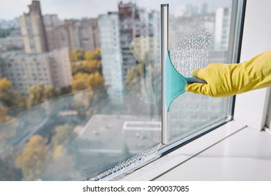 Gloved hand washing windowpane using implement with rubber blade