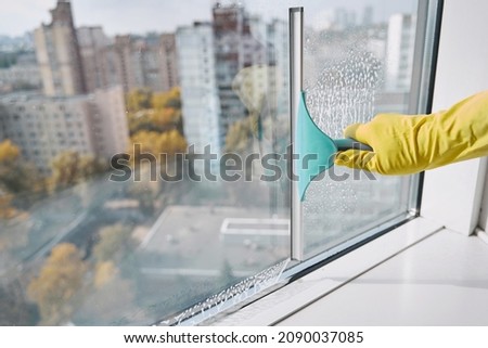 Gloved hand washing windowpane using implement with rubber blade