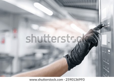 Gloved hand worker operating machine control panel in modern bakery factory setting.