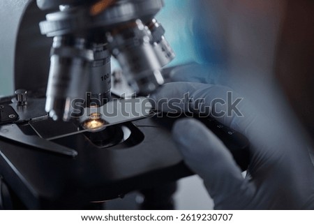 Gloved hands adjusting microscope in laboratory setting showing precision needed for scientific research and analysis