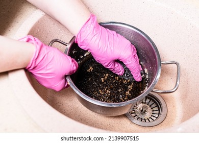 gloved hands clean saucepan with burnt food with metal sponge in pink sink at home kitchen - Shutterstock ID 2139907515