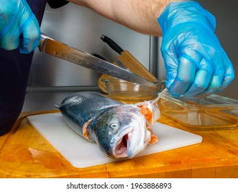 The Gloved Hands Of The Cook Cut Off The Fins On The Salmon Carcass With A Knife. Cutting Fresh Fish In The Kitchen On A Cutting Board.