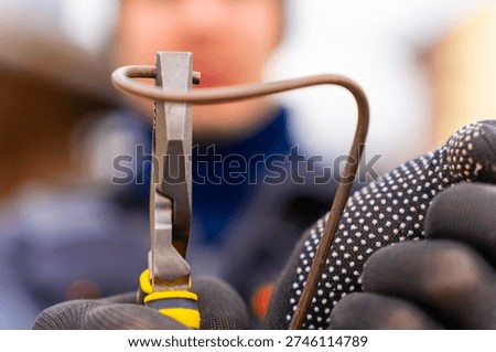 Gloved hands cutting solid copper wire with pliers, metal jaws gripping and bending electrical conductor during manual repair work.