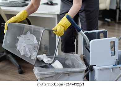 Gloved Hands Of Female Cleaner Throwing Trash From Garbage Bin Into Plastic Bucket On Janitor Trolley While Working In Modern Office