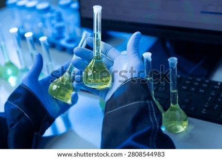 Gloved hands holding multiple volumetric flasks with yellow solution.