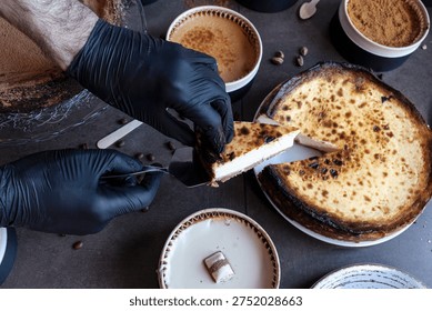 Gloved hands serving a portion of homemade baked cheesecake on a dark grey background