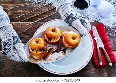 Gloved hands serving spicy baked apple dessert with cinnamon on a metal plate at a winter BBQ with snow on the table
