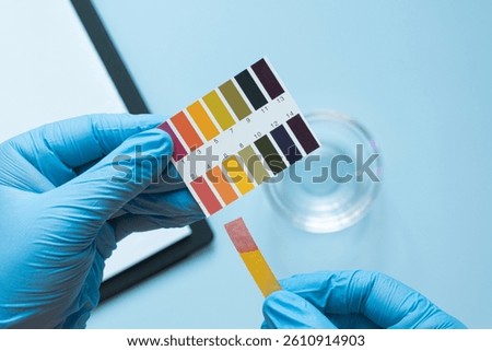 Gloved hands testing ph level with color chart and strips in laboratory setting. Acidic pH environment.