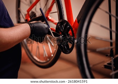 Gloved hands use a tool to attach a crank arm to a red bikes bottom bracket, focusing on precise mechanical assembly.