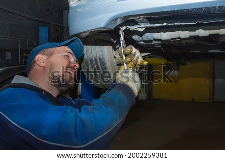 A gloved mechanic uses a key to align the curved part of the car's body. the machine is hanging on a hydraulic lift. Car service business concept